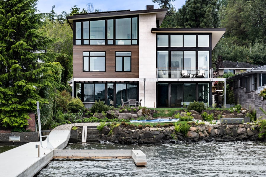 An exterior shot of a contemporary home with a combination of siding types, large expanses of glass, and a lakeside location.