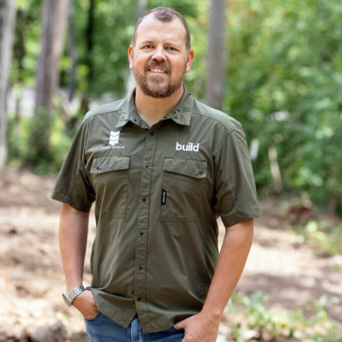 Jake Bruton stands in a forest wearing a green button-up