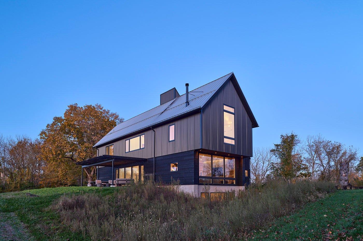 A twilight shot of a home with metal and shou sugi ban siding and large glass expanses surrounded by a meadow.