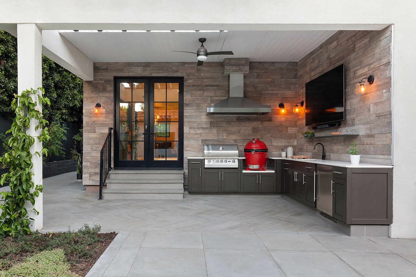 An exterior shot of an outdoor kitchen featuring a black E-Series Hinged Patio Door with inswing, traditional panels, and colonial grilles.