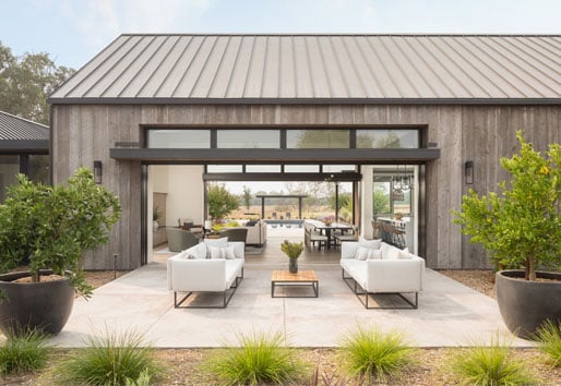 An exterior shot of a black Andersen® MultiGlide™ Door that opens an entire wall to provide a seamless indoor/outdoor space between living room and courtyard.