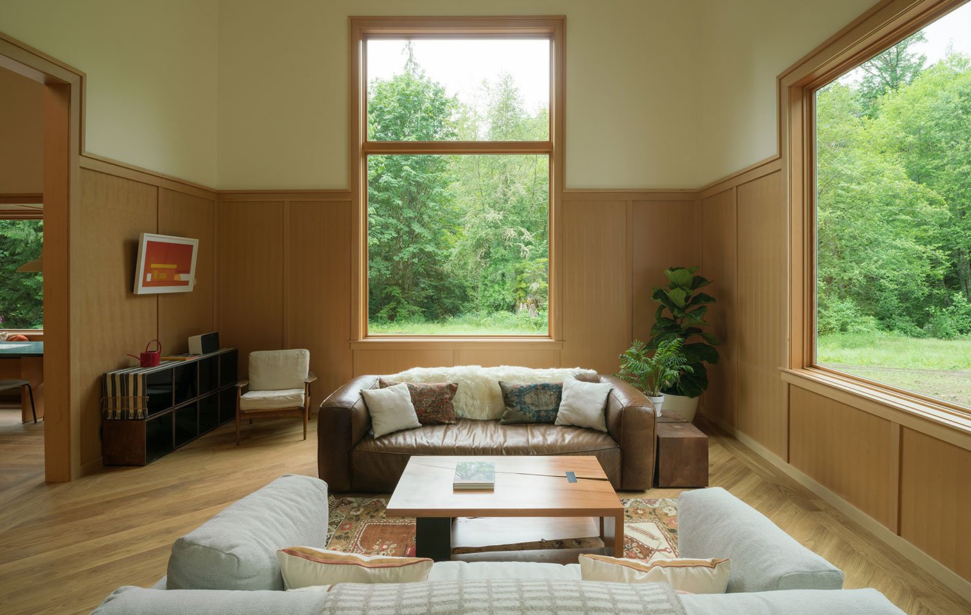 A living room with two monumental E-Series Picture Windows that integrate with the wood paneling on the walls.