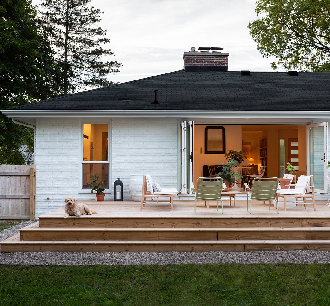house painted white with large patio doors leading to a wooden porch with steps and outdoor furniture