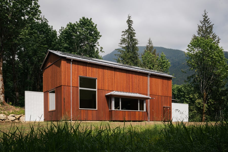 A home surrounded by woods and mountains with vertical cedar cladding and a large bay window.