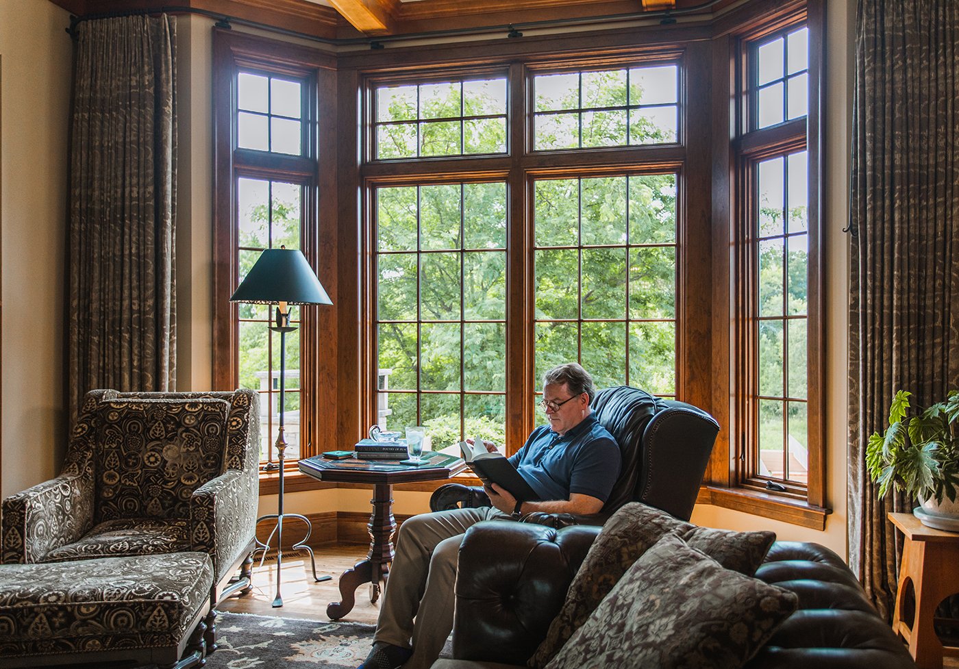A living room with a large walk-out bay window composed of Andersen® A-Series Casement Windows with dark stained wood frames.