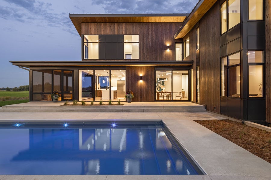 A contemporary home with cedar cladding and black floor-to-ceiling windows forms an L-shape around the backyard pool.