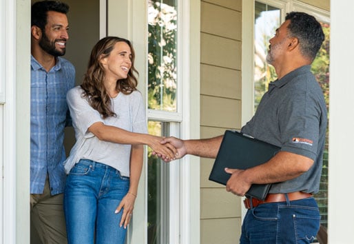 A man and woman stand in their front door greeting a contractor who is standing on their porch.