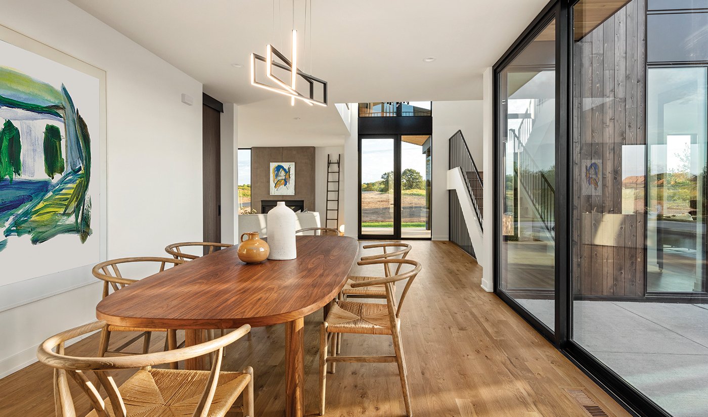 A dining room with hardwoods floors, a wood table with cane-bottomed chairs and a MultiGlide™ Door with black frames.