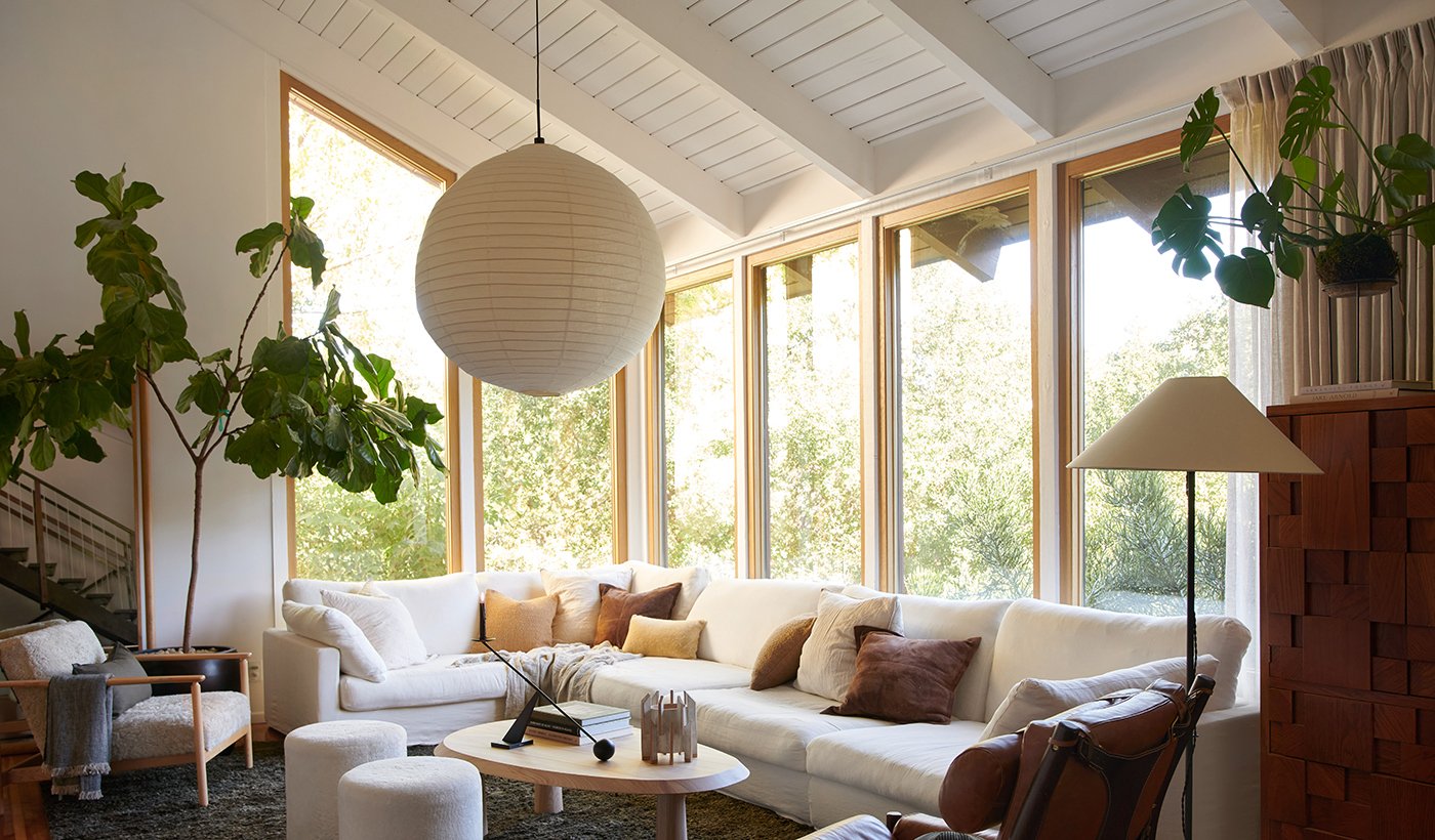 A living room with a large white couch and chairs, dark gray rug and a wall of picture windows with white oak frames.