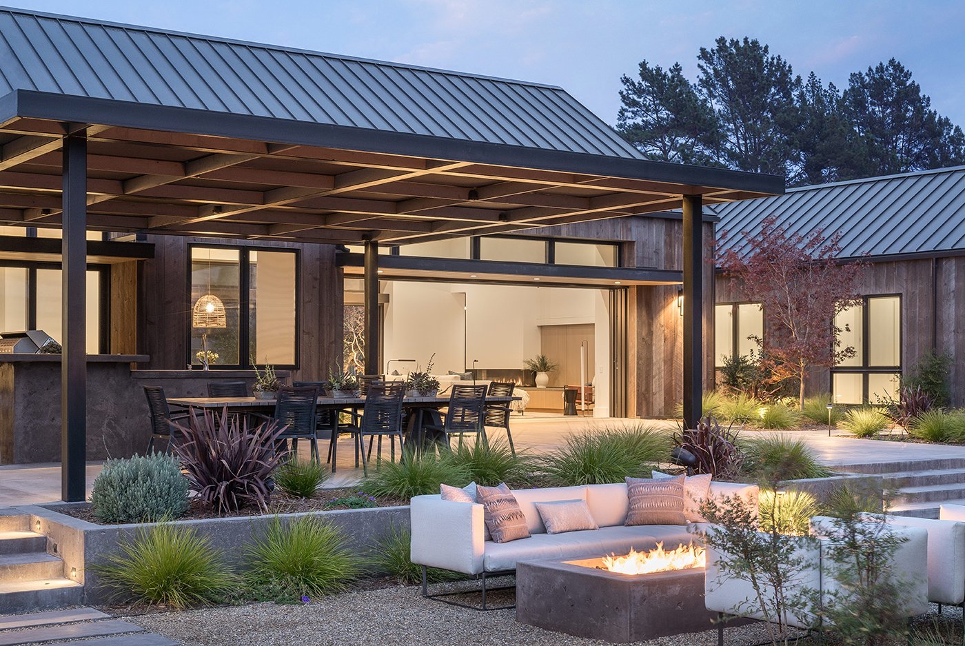 An exterior shot of a home designed for outdoor living with a wall-sized MultiGlide™ Door that blurs the line between in and outdoors and amenities like and outdoor kitchen, outdoor dining space, and outdoor living room.