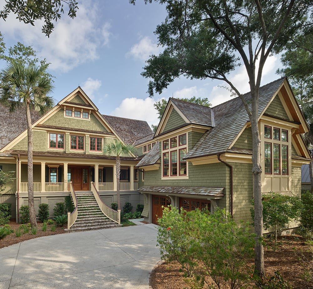 A multiple-story house with green shingle siding and steeply pitched gray shingle roof, with colonial grille patterns on the windows.