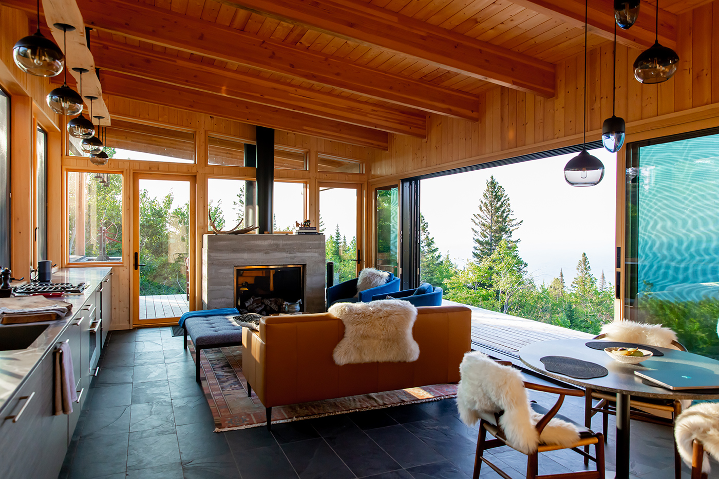 Interior view of a modern cabin with large, glass Andersen windows nestled in the north woods and an Andersen MultiGlide Door opening an entire wall to the landscape and Lake Superior views beyond. 