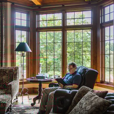 A living room with a large walk-out bay window composed of Andersen® A-Series Casement Windows with dark stained wood frames.